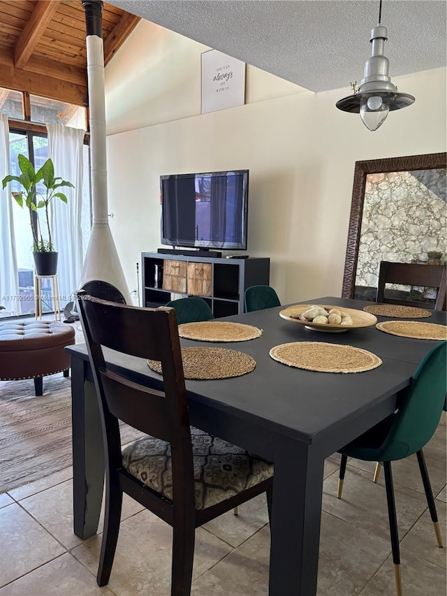 dining space featuring tile patterned flooring, a wood stove, a textured ceiling, and lofted ceiling with beams