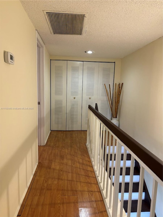 hallway with an upstairs landing, visible vents, a textured ceiling, and dark wood-type flooring