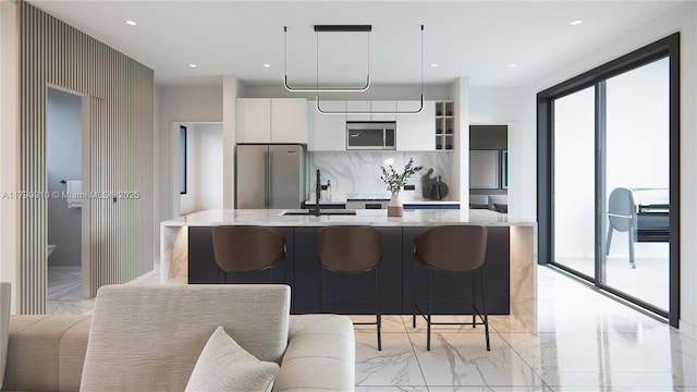 kitchen with appliances with stainless steel finishes, a sink, marble finish floor, white cabinetry, and a center island with sink