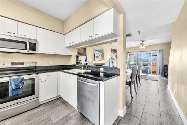 kitchen featuring a ceiling fan, appliances with stainless steel finishes, dark countertops, a sink, and white cabinets
