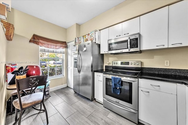 kitchen featuring stainless steel appliances, dark countertops, white cabinetry, and baseboards