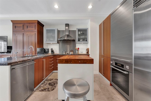 kitchen featuring glass insert cabinets, butcher block countertops, wall chimney range hood, a sink, and stainless steel appliances