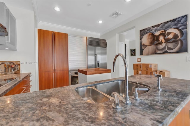 kitchen with a sink, built in refrigerator, brown cabinets, and visible vents