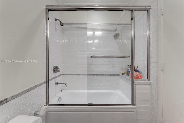 bathroom featuring bath / shower combo with glass door, toilet, and tile walls