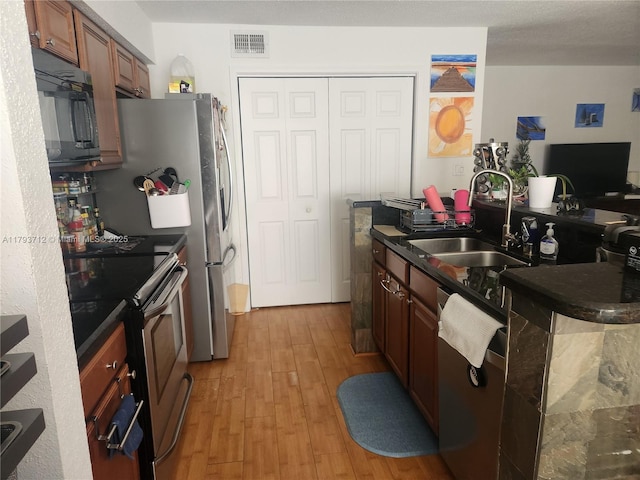 kitchen featuring visible vents, dark countertops, a sink, light wood-style flooring, and appliances with stainless steel finishes