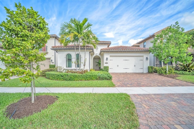 mediterranean / spanish house featuring a tile roof, decorative driveway, a front lawn, an attached garage, and stucco siding