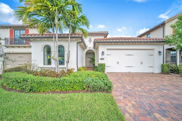 mediterranean / spanish-style home with an attached garage, decorative driveway, stucco siding, and a tiled roof