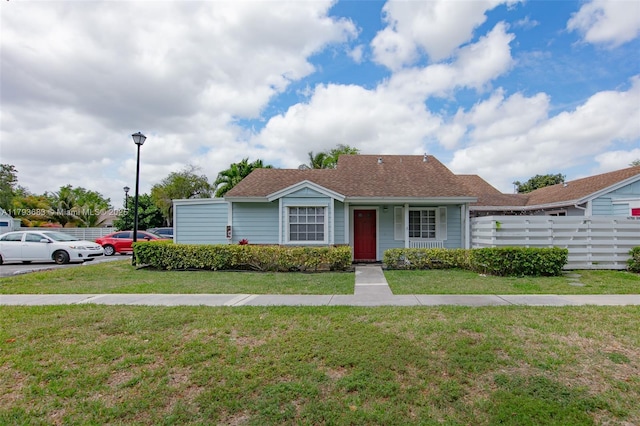 view of front of home featuring roof with shingles, fence, and a front yard