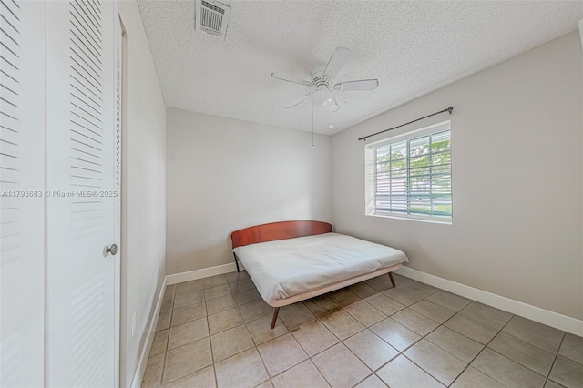 bedroom with a ceiling fan, a textured ceiling, visible vents, light tile patterned floors, and baseboards