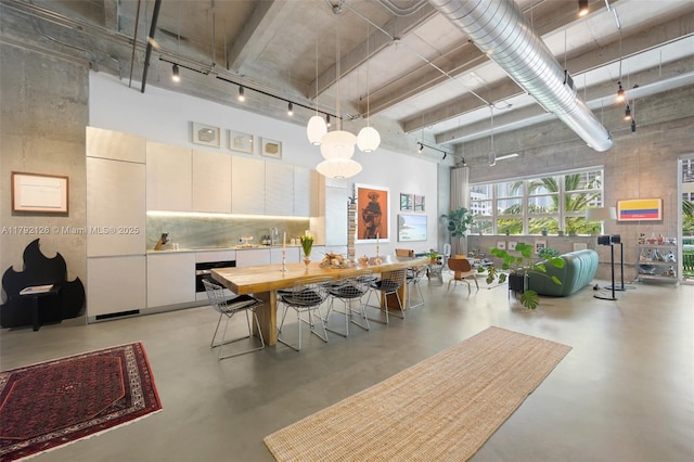 dining room featuring finished concrete flooring, track lighting, and a towering ceiling