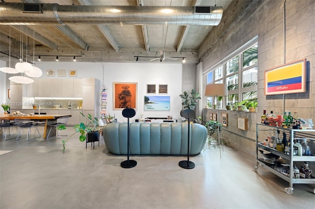 living room featuring concrete flooring, visible vents, track lighting, and a towering ceiling