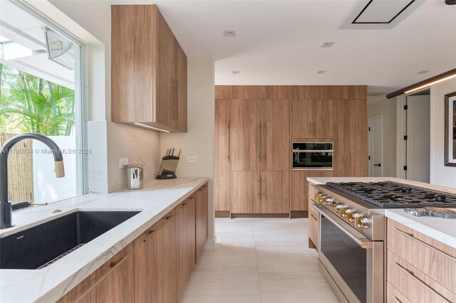 kitchen with high end stove, a sink, modern cabinets, and light stone countertops