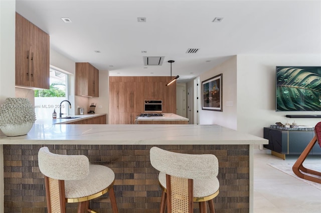 kitchen with brown cabinetry, a peninsula, stainless steel oven, a kitchen bar, and a sink