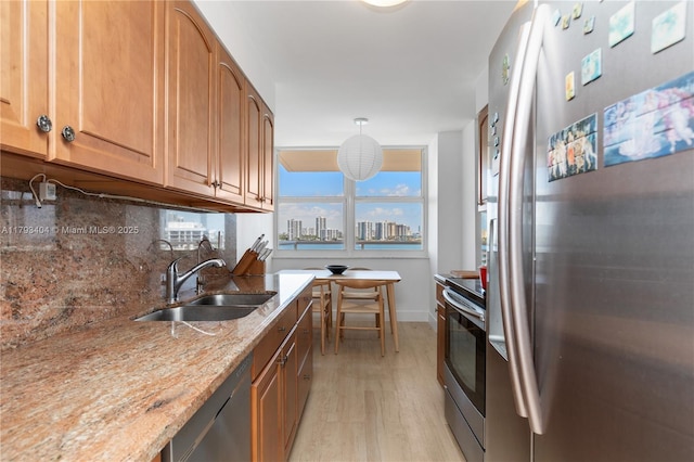 kitchen with light stone countertops, a sink, light wood-style floors, stainless steel appliances, and backsplash