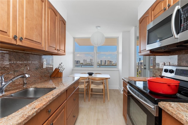 kitchen with tasteful backsplash, a sink, light stone counters, stainless steel appliances, and light wood-style flooring