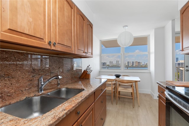 kitchen with light stone countertops, baseboards, light wood-type flooring, a sink, and backsplash