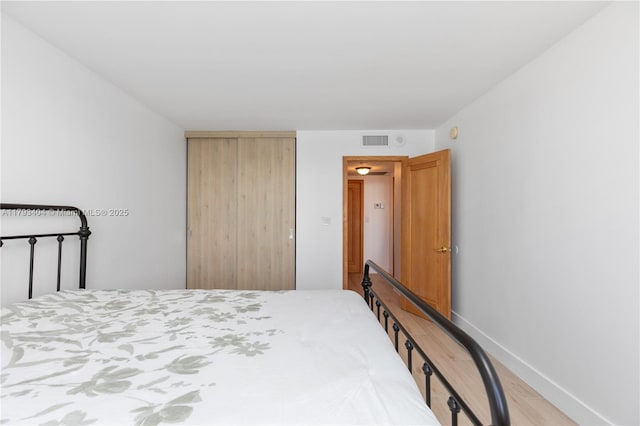 bedroom featuring visible vents, baseboards, wood finished floors, and a closet
