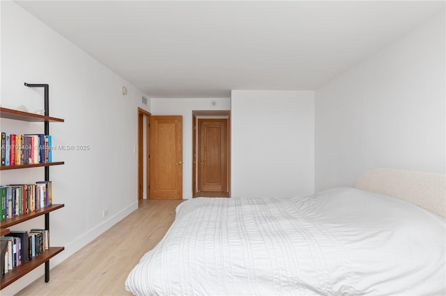 bedroom with baseboards, light wood finished floors, and visible vents