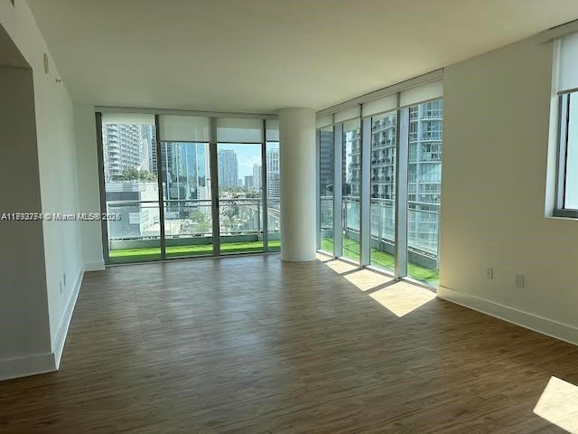 empty room featuring baseboards, a city view, wood finished floors, and a wall of windows