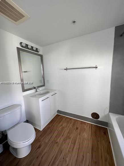 full bath with a bath, visible vents, wood finished floors, vanity, and toilet
