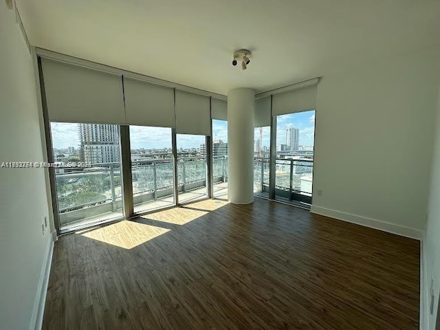 spare room featuring baseboards, floor to ceiling windows, a city view, and dark wood-style floors