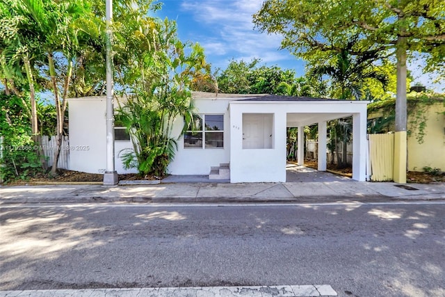 view of front of home with fence, a carport, and stucco siding