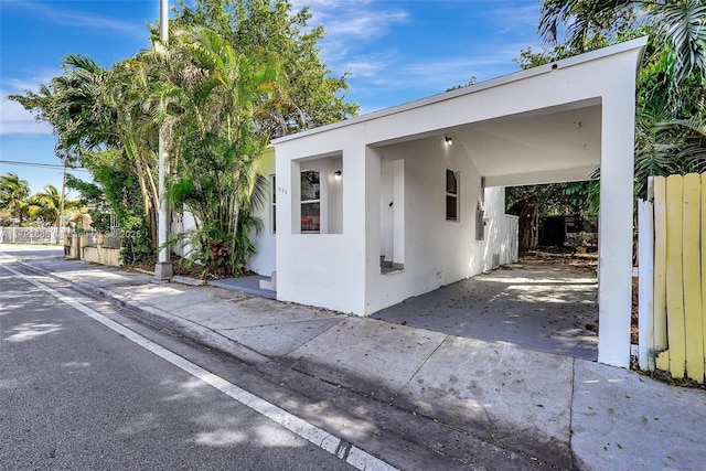 view of front of home with fence, stucco siding, an attached carport, and driveway