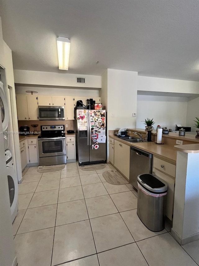 kitchen featuring appliances with stainless steel finishes, a sink, a peninsula, stacked washer / dryer, and visible vents