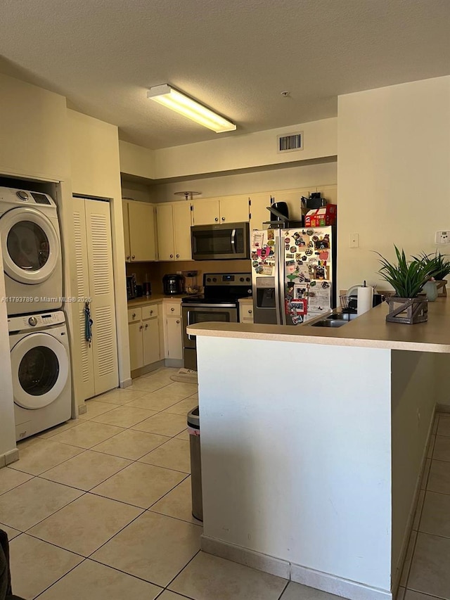 7270 NW 114th Ave Unit 203-9, Doral, FL 33178 - kitchen featuring appliances with stainless steel finishes, a peninsula, light tile patterned floors, visible vents, and stacked washer and clothes dryer