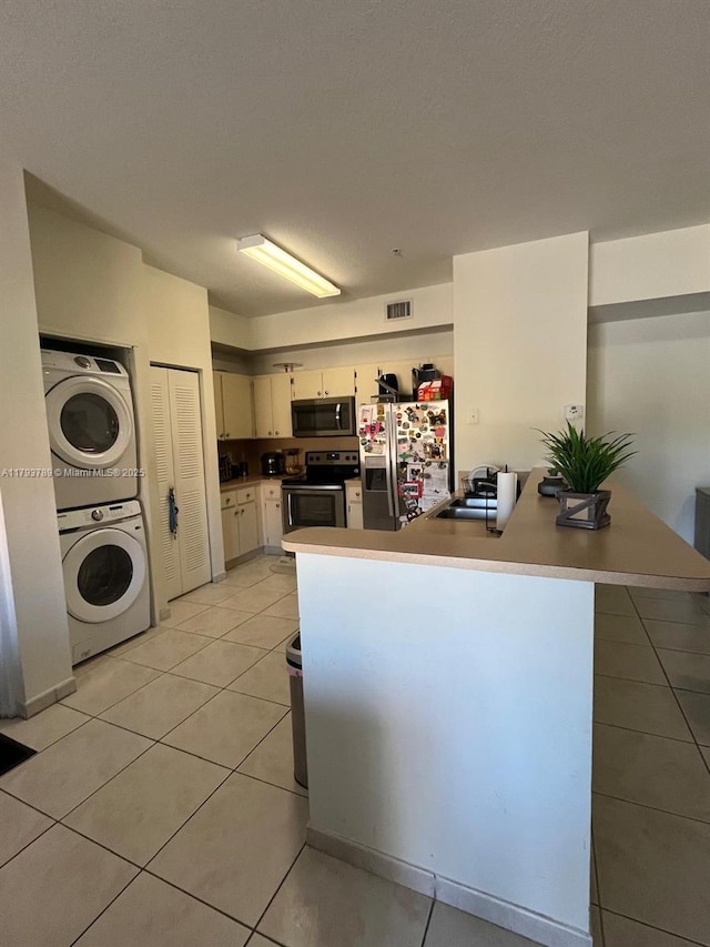 kitchen with stacked washer and dryer, visible vents, appliances with stainless steel finishes, a sink, and a peninsula