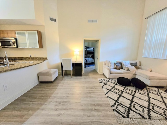 living room with visible vents, baseboards, a towering ceiling, and wood finished floors