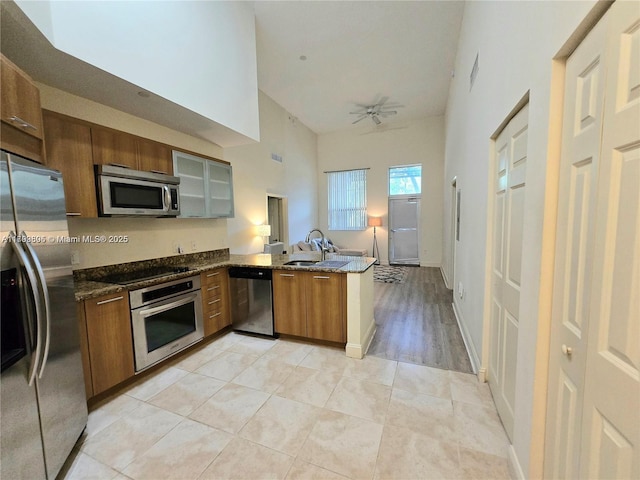 kitchen featuring brown cabinets, a sink, high vaulted ceiling, stainless steel appliances, and a peninsula