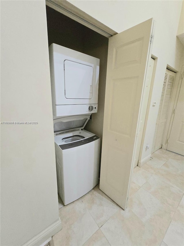 laundry area with laundry area, stacked washer and dryer, baseboards, and light tile patterned floors