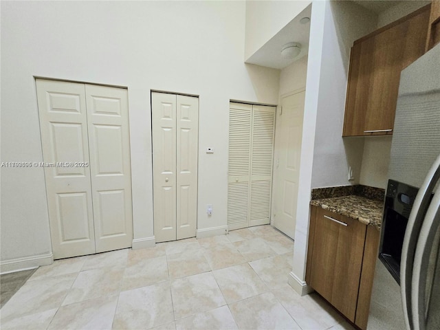 kitchen featuring dark stone counters, light tile patterned flooring, refrigerator with ice dispenser, and baseboards