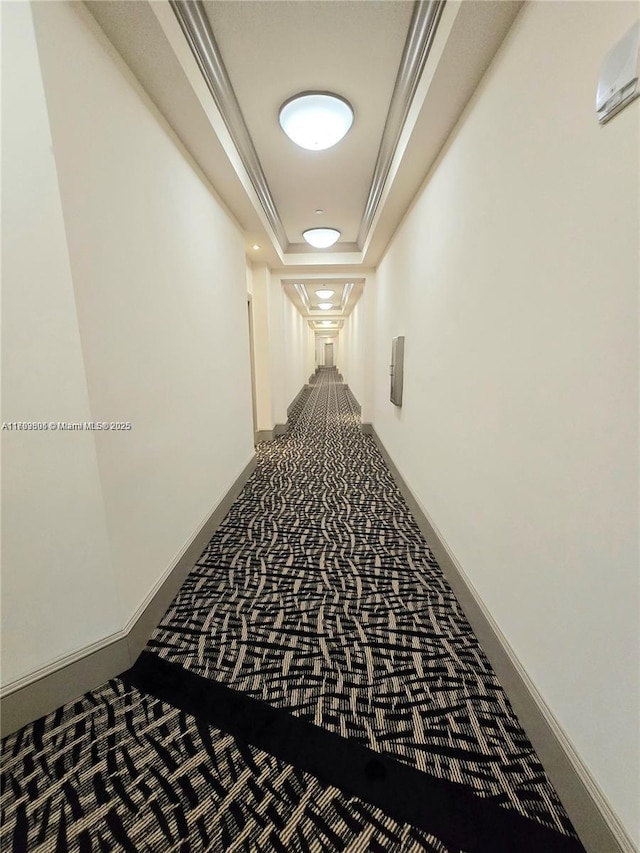 hallway with baseboards, ornamental molding, carpet, and a tray ceiling