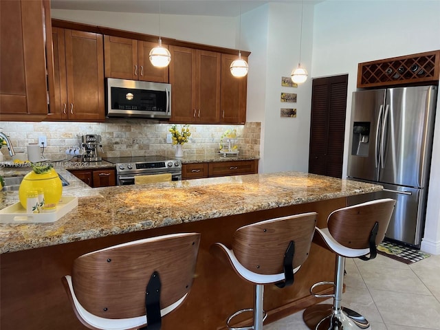 kitchen with light stone countertops, a kitchen bar, a sink, appliances with stainless steel finishes, and backsplash