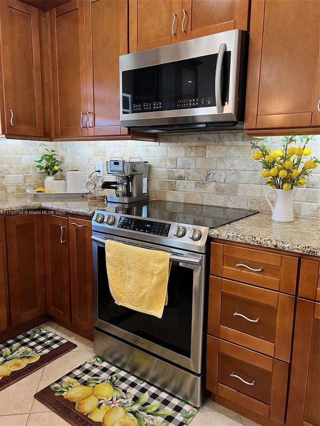 kitchen featuring brown cabinets, light stone countertops, appliances with stainless steel finishes, decorative backsplash, and light tile patterned floors