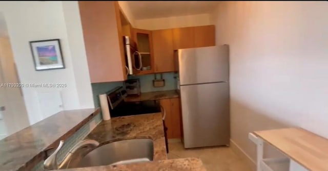 1881 Washington Ave Unit 8C, Miami Beach, FL 33139 - kitchen with appliances with stainless steel finishes, brown cabinets, light stone counters, a sink, and glass insert cabinets
