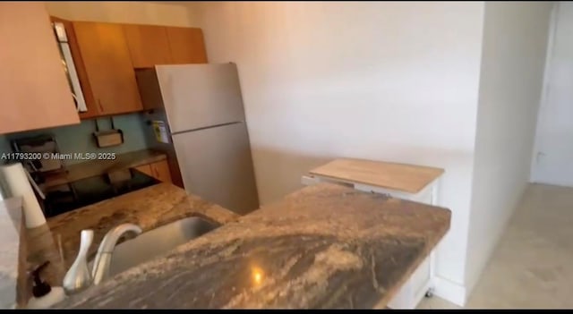 1881 Washington Ave Unit 8C, Miami Beach, FL 33139 - kitchen featuring freestanding refrigerator, light stone countertops, brown cabinetry, and a peninsula