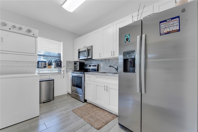kitchen with white cabinetry, tasteful backsplash, a sink, appliances with stainless steel finishes, and stacked washer / drying machine