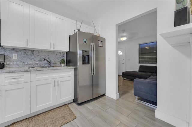 kitchen with a sink, light stone counters, stainless steel refrigerator with ice dispenser, and white cabinetry