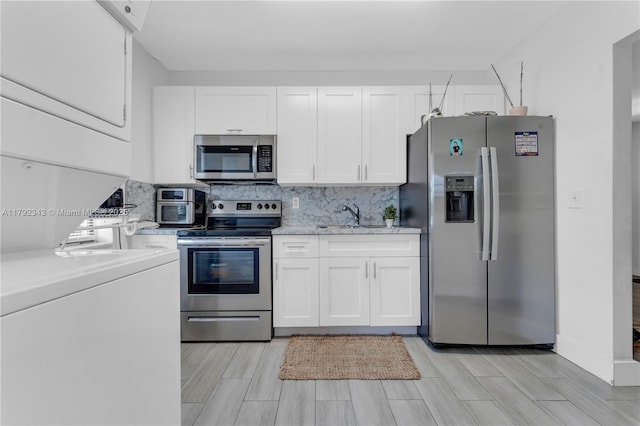 kitchen featuring stacked washer / drying machine, a sink, stainless steel appliances, white cabinetry, and decorative backsplash