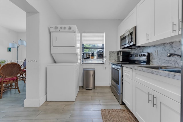 kitchen with backsplash, appliances with stainless steel finishes, stacked washer / drying machine, a sink, and white cabinets