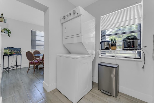 laundry area featuring laundry area, stacked washing maching and dryer, plenty of natural light, and baseboards