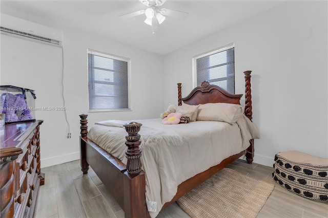 bedroom with baseboards, ceiling fan, a wall unit AC, and wood finished floors