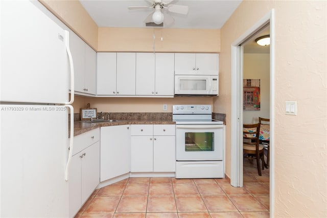 kitchen with dark countertops, a sink, white appliances, white cabinetry, and a ceiling fan