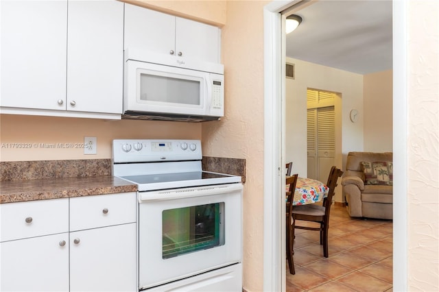 kitchen with white appliances, white cabinetry, dark countertops, and light tile patterned floors