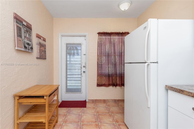 kitchen with freestanding refrigerator, a textured wall, light tile patterned flooring, and white cabinets