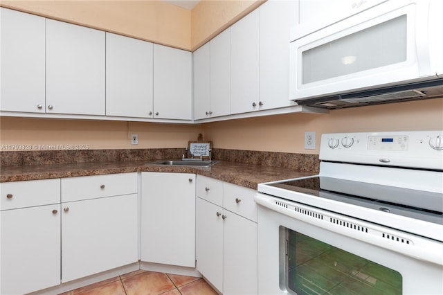 kitchen with light tile patterned flooring, dark countertops, white appliances, white cabinets, and a sink