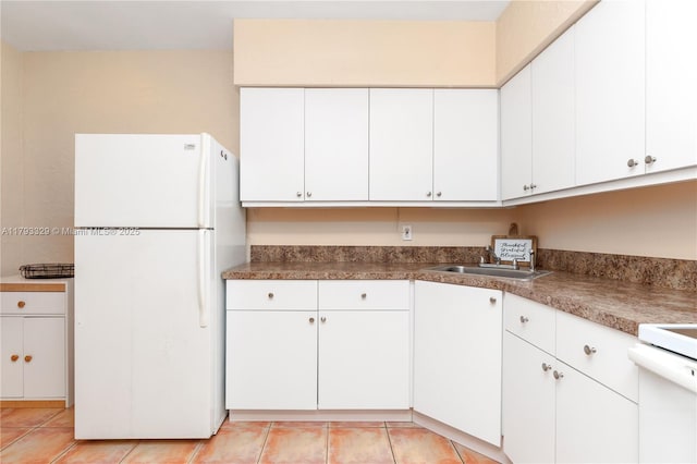 kitchen with a sink, light tile patterned floors, white cabinets, and freestanding refrigerator